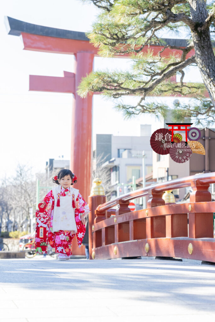 鎌倉の鶴岡八幡宮に七五三のお参り 出張撮影 ピンクの着物を着て千歳飴を持った3歳の女の子と鳥居